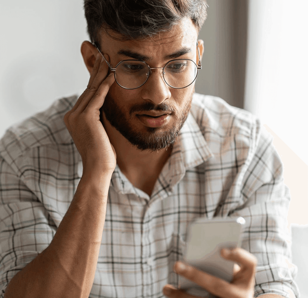 Homem olhando para o celular pensativo.