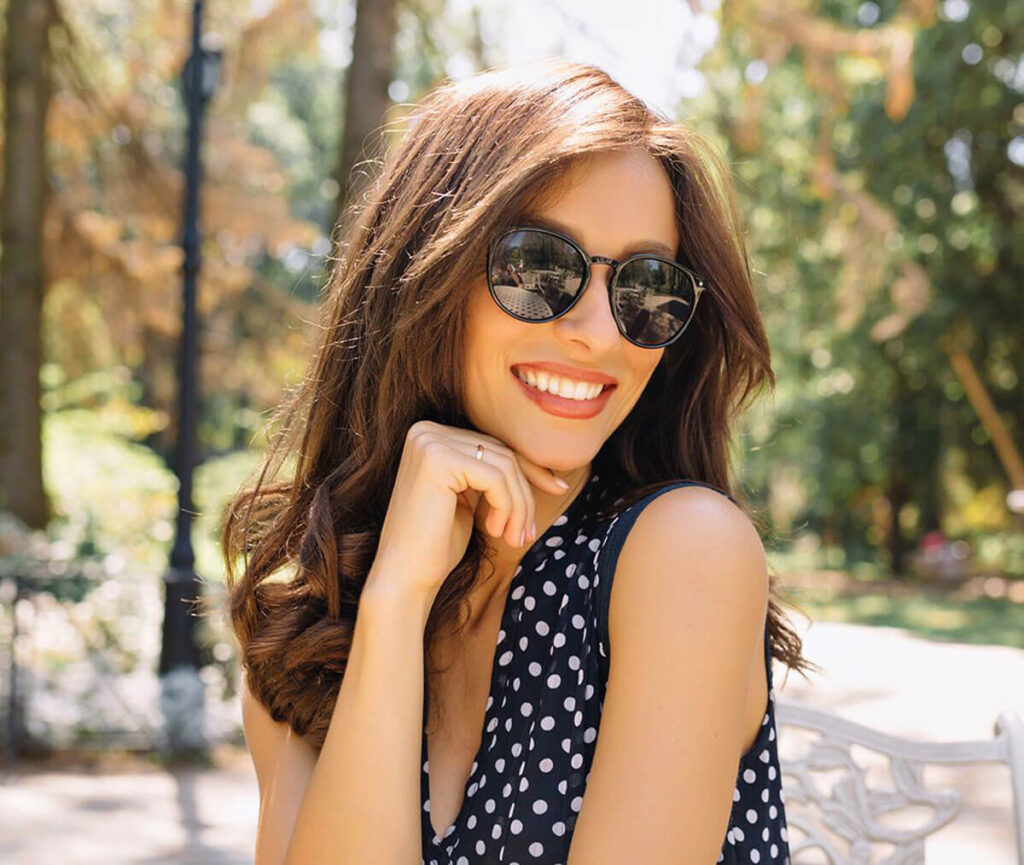 Mulher em parque com vestido poá e óculos de sol.